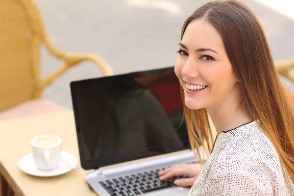 Happy woman using a laptop in a restaurant and looking at camera