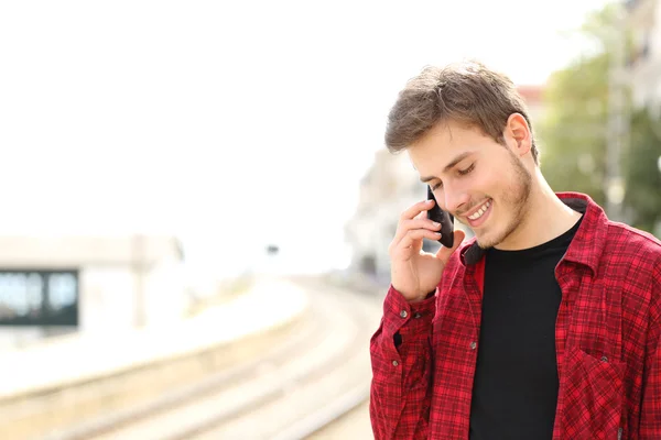 Teen guy calling on the mobile phone waiting a train