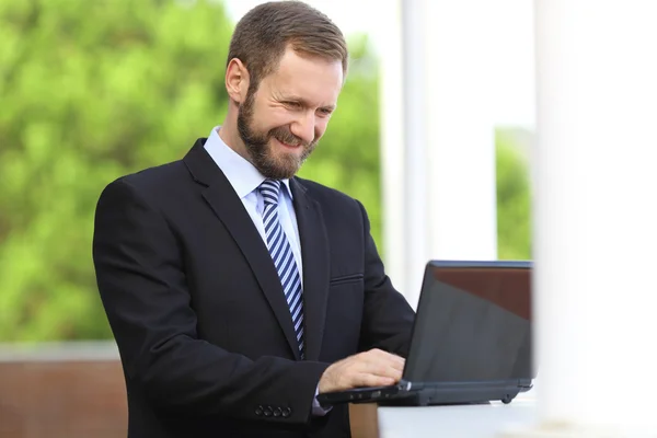 Happy business man working browsing internet in a laptop outdoor