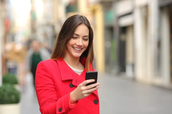 Girl walking and texting on the smart phone in the street in red