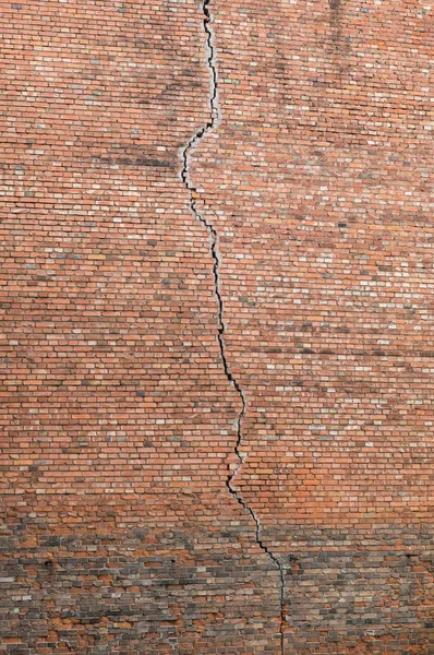 Long vertical crack in a red brick wall