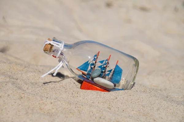Small ship in the glass bottle lying in the sand