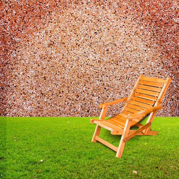 Wooden deck chair on green grass with stone wall background