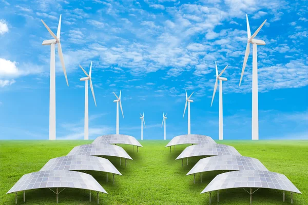 Solar panels and wind turbine on green grass field against blue