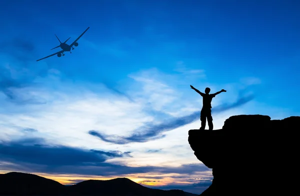 Silhouette of a man on the rock and silhouette commercial plane