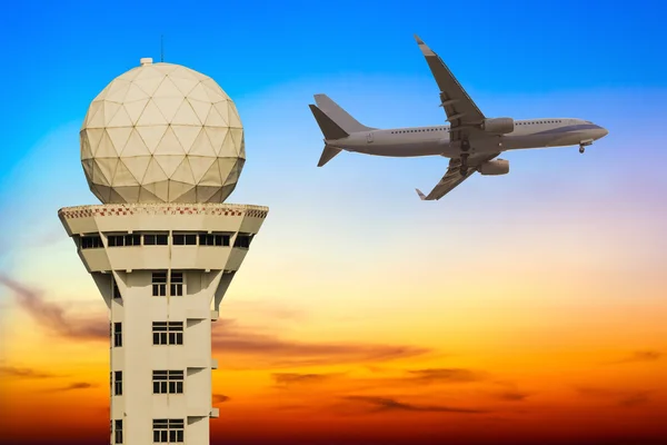 Commercial airplane flying over airport control tower at sunset