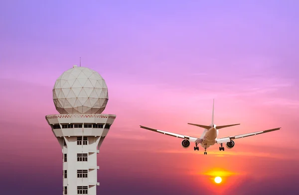 Airport control tower and commercial airplane landing at sunset