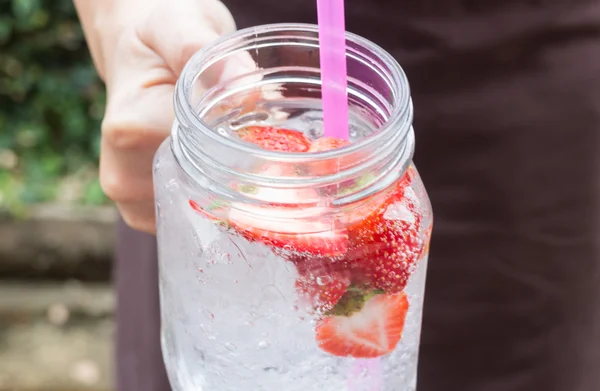 Hand on serving glass of iced strawberry soda drink