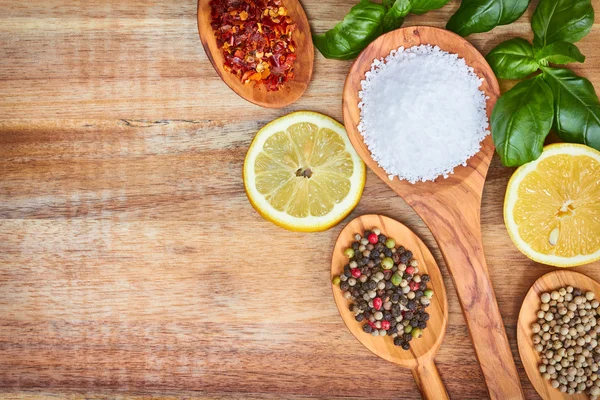 Spices, lemon basil and sea salt in spoons on wooden background