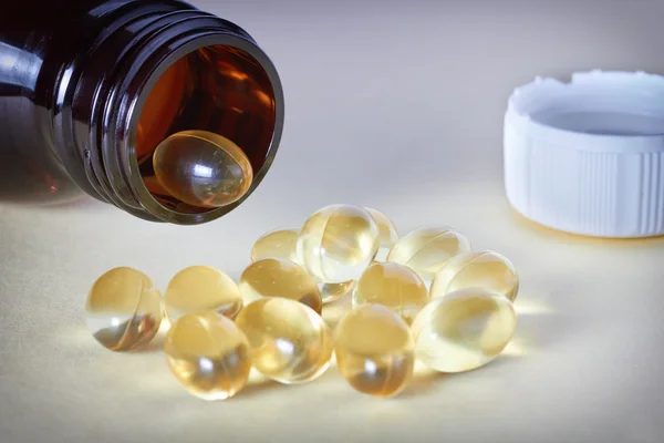 Oil pills spilling out of prescription bottle on table backgroun