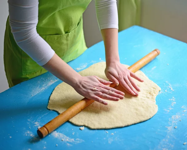 Hands baking dough with rolling pin on table