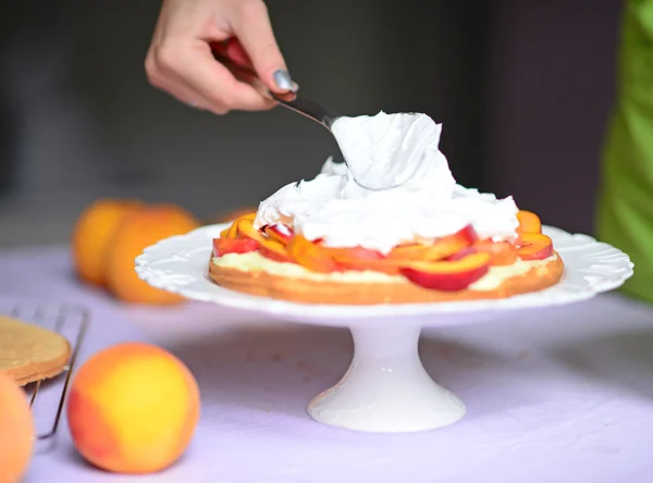 Woman hand put whipped cream on peach cake