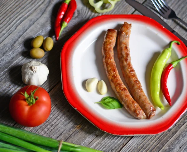 Portion of sausages on plate with tomatoe, fresh onion, chilly p