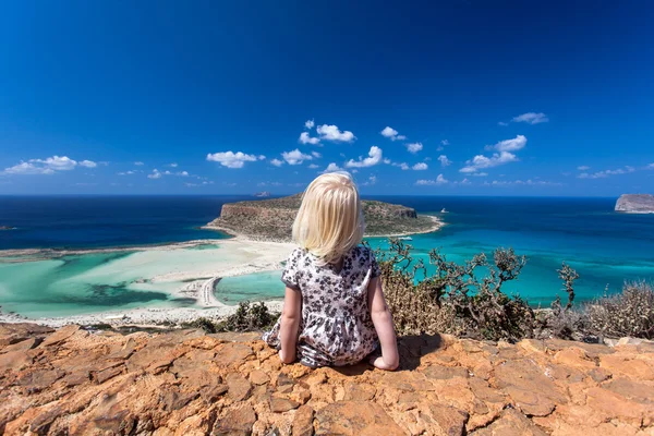 Cute girl sitting on a rock facing Balos beach and Gramvousa island on Crete, Greece