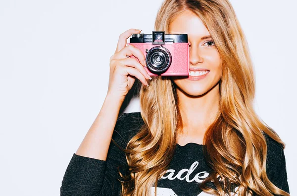Beautiful Hipster woman taking photos with pink retro film camera on white background. Close up. Indoor. Warm color.