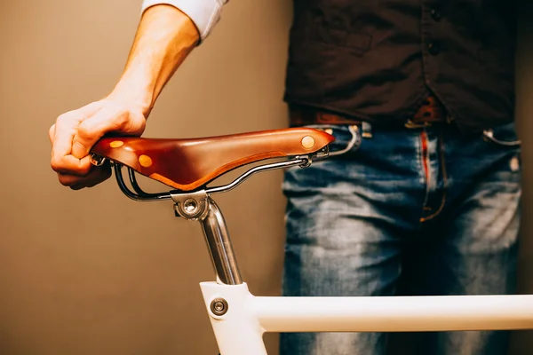 Close-up of young hipster man holding hands on his bicycle while standing indoors. Warm color.