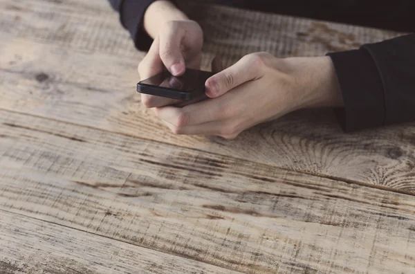 Close up of male hands holding smartphone and pointing finger to graph and text on screen at table wooden planks. Hipster style. Free space for text.