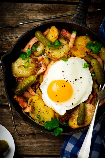 Country breakfast from potatoes, with bacon and fried eggs in a pig-iron frying pan.