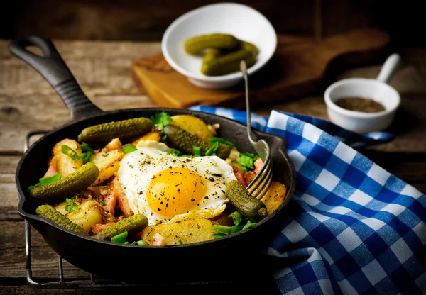 Country breakfast from potatoes, with bacon and fried eggs in a pig-iron frying pan.