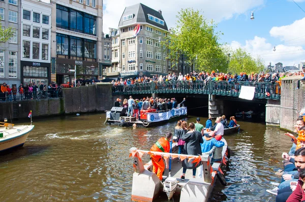 AMSTERDAM-APRIL 27: Boat paty on the Singel canal, crowd of people on the bridge on King\'s Day on April 27,2015.
