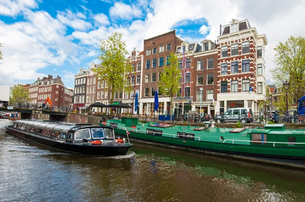 Boat trip through Amsterdam canals with houseboats along the canal, people enjoy sightseeing, Netherlands.