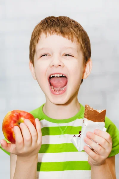 Child chooses chocolate or apple on a light background in the st