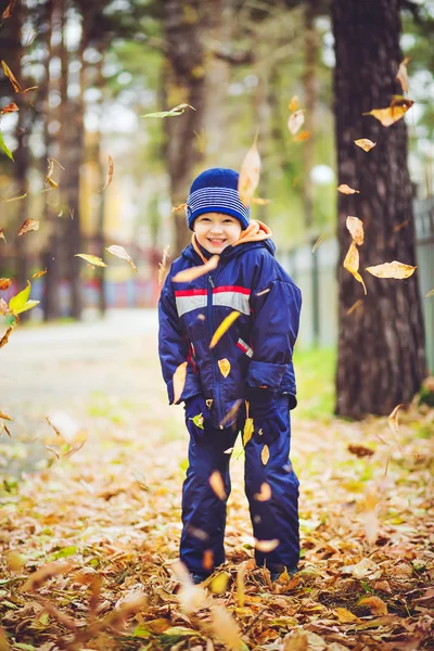 Happy little boy throws the autumn leaves in the air.