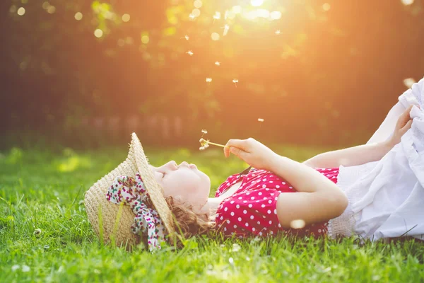 The child lays on a grass and blowing dandelion in the rays of t