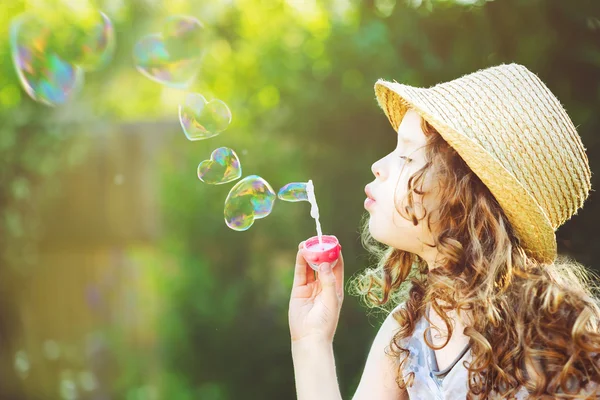 Cute girl blowing soap bubbles in a heart shape.