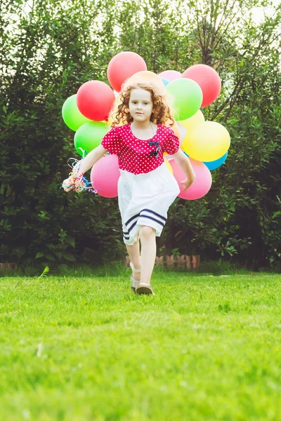 Little curly girl running with colored balloons. Happy childhood