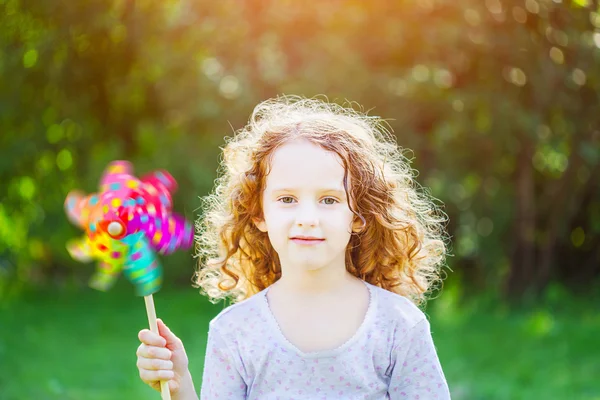 Little girl with rainbow pinwheel toy in summer park. Eco, trave