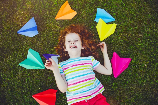 Laughing girl throwing paper airplane in green grass at summer p