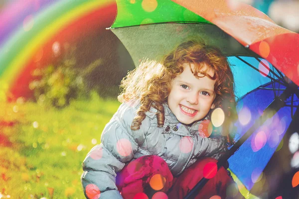 Laughing girl in the rain with a rainbow and with color bokeh.