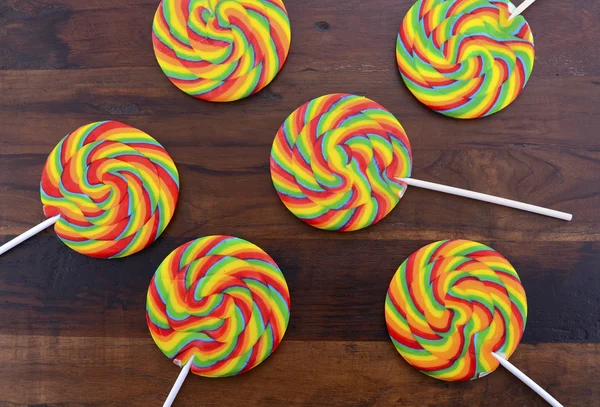 Bright rainbow lollipop candy on dark wood table.