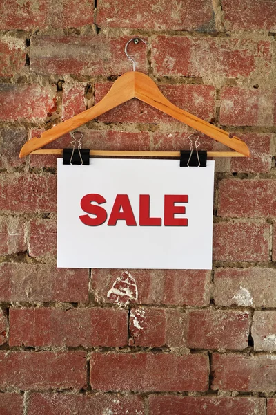Sale sign on coat hanger against brick wall
