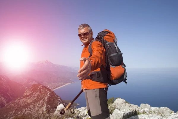 Hikers climbing on rock, mountain at sunset, one of them giving hand and helping to climb.