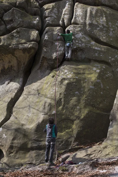 Young man climbs on a cliff with a rope.