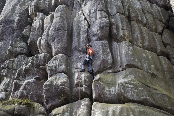 Young man climbs on a cliff with a rope.