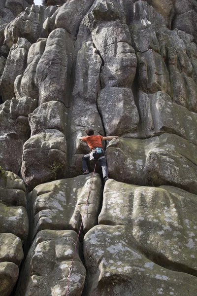 Young man climbs on a cliff with a rope.
