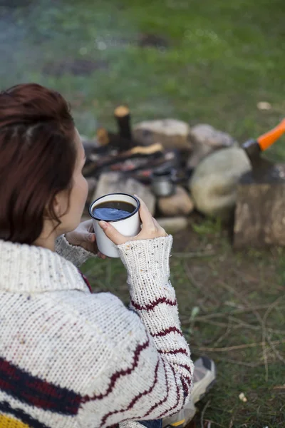 Girl sitting near a campfire at the campsite looking at map and drinking coffee.
