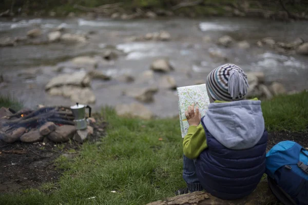 Teenager sitting near a fire in camping and watching map.