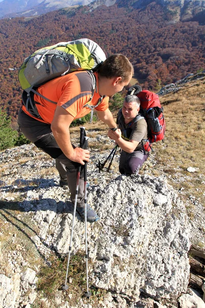 Man giving helping hand to friend to climb mountain rock cliff.