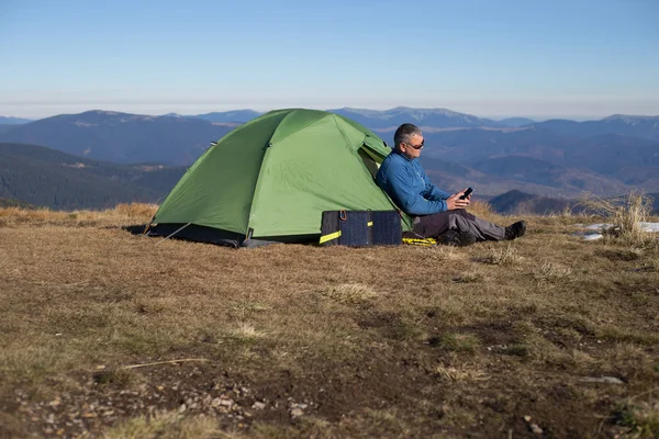 The solar panel attached to the tent. The man sitting next to mobile phone charges from the sun.