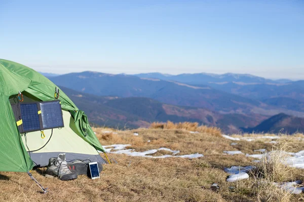 The solar panel attached to the tent. The man sitting next to mobile phone charges from the sun.