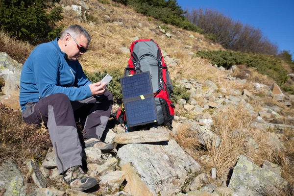 The solar panel attached to the tent. The man sitting next to mobile phone charges from the sun.