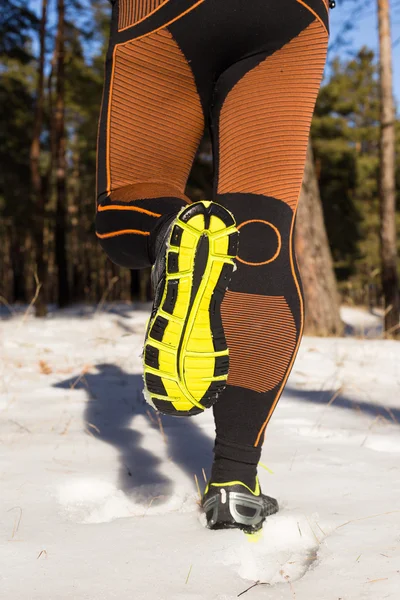 Winter trail running: man takes a run on a snowy mountain path in a pine woods.