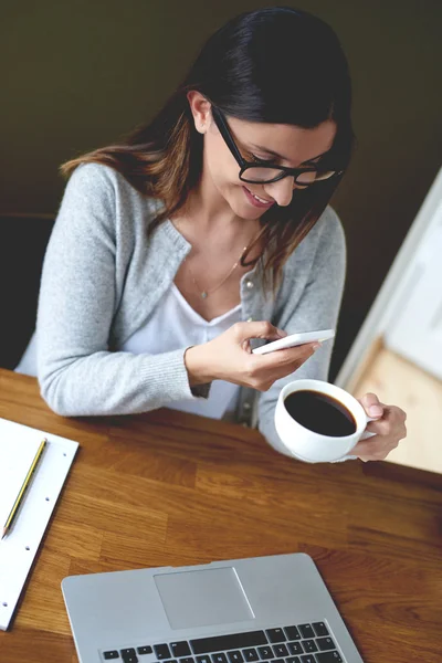 Woman smiling while checking phone and drinking coffee