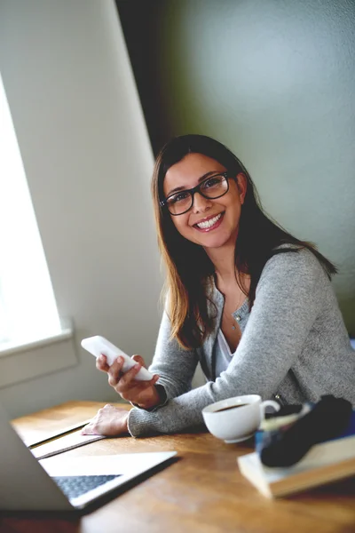 Woman sitting in home office smiling and holding mobile phone