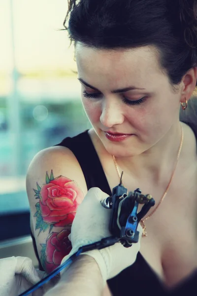 Tattooer showing process of making a tattoo on young beautiful hipster woman with red curly hair