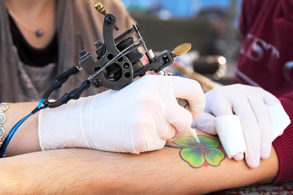 Tattooer showing process of making a tattoo. Tattoo design in the form of four-leaf clover